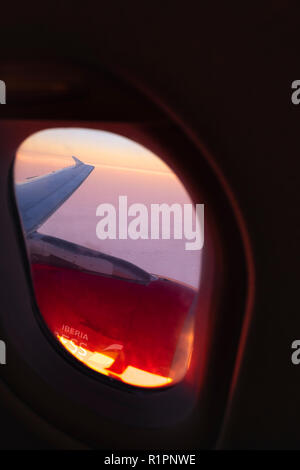 La fenêtre de l'avion sur l'aile et le moteur sur un vol Iberia Express avec le lever du soleil illuminant les nuages. Banque D'Images