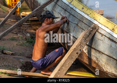 Don Det, Laos - 22 Avril 2018 : l'homme Local la réparation d'un bateau en bois cassée sur les rives du Mékong en 4000 Islands Banque D'Images