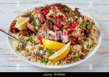 Tendershoulder d'agneau rôti lentement tomber en morceaux tendres servis avec salade de couscous au persil, parsemé de graines de grenade sur un plateau blanc avec cuillère Banque D'Images