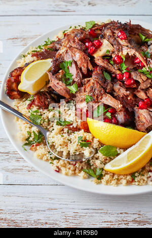 Rôti lentement tomber en morceaux tendres servis avec salade de couscous au persil, parsemé de graines de grenade et de feuilles de menthe sur un plateau blanc avec une cuillère, Banque D'Images