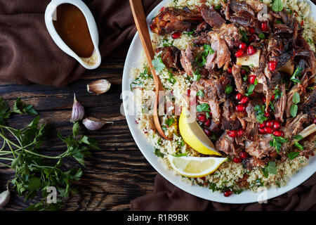 Vue de dessus de la viande rôtie lentement tomber en morceaux servis avec salade de couscous au persil, parsemé de graines de grenade, les feuilles de menthe sur un plateau blanc avec Banque D'Images