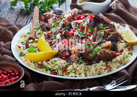 L'agneau rôti lentement tomber en morceaux de viande servis avec salade de couscous au persil, parsemé de graines de grenade, les feuilles de menthe sur un plateau blanc avec la sauce sur un Banque D'Images