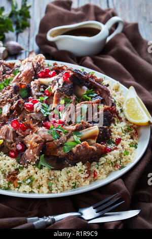 L'agneau rôti lentement tomber en morceaux de viande servis avec salade de couscous au persil, parsemé de graines de grenade, les feuilles de menthe sur un plateau blanc avec la sauce sur un Banque D'Images