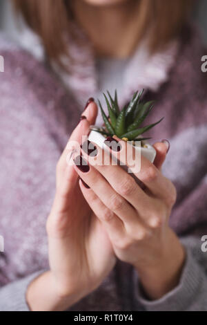 Fille avec manucure bourgogne tenant un pot avec une fleur Banque D'Images