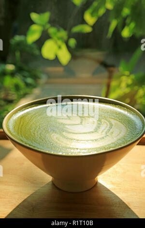 Tasse de thé vert japonais Matcha Latte avec Art dans la lumière du soleil, les plantes vertes floues en arrière-plan Banque D'Images