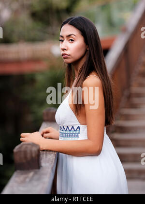 Belle fille brune en robe blanche à l'écart dans le parc Banque D'Images