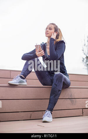 Jeune femme sportive fit se reposer et écouter la musique sur téléphone mobile après la formation en environnement urbain en plein air Banque D'Images