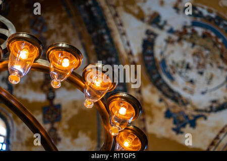 Partie d'un lustre électrique moderne avec lumière chaude en face d'un plafond peint floue dans un bâtiment historique Banque D'Images