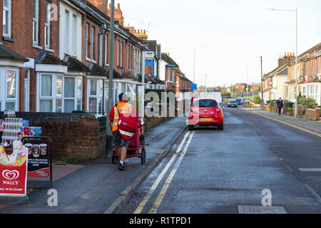 Royal Mail facteur poussant un chariot de poste en short en hiver, le long d'une route victorienne avec terrasse, Ashford, Kent, UK Banque D'Images