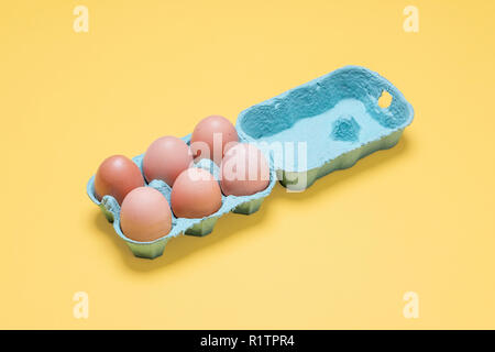 Demi-douzaine d'oeufs en carton brun organique. Six oeufs bruns dans la caisse contenant sur un fond jaune pastel Banque D'Images