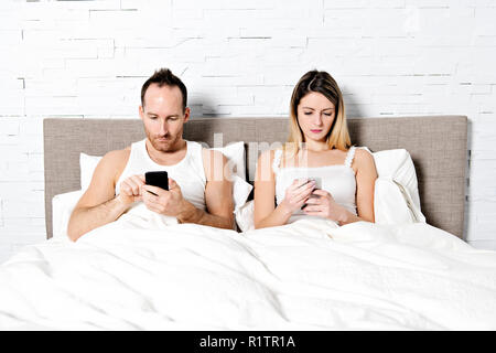 Un couple en utilisant leur téléphone mobile au lit Banque D'Images