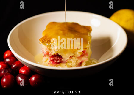 Tranche de gâteau aux canneberges arrosé de sauce au citron dans des bol blanc avec des canneberges fraîches et de citron sur les côtés. Photo de paysage avec dos noir Banque D'Images