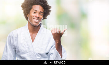 South American man wearing kimono karaté sur fond isolé avec sourire heureux face à la recherche et en pointant sur le côté avec le pouce vers le haut. Banque D'Images