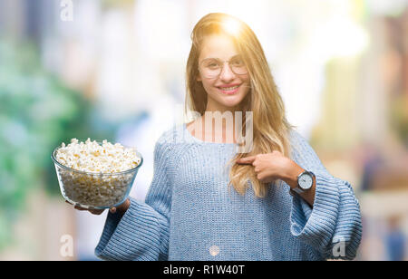 Jeune belle blonde woman eating popcorn sur fond isolé avec surprise face à face à lui-même Banque D'Images