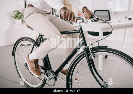 Portrait of african american businessman riding bicycle in office Banque D'Images