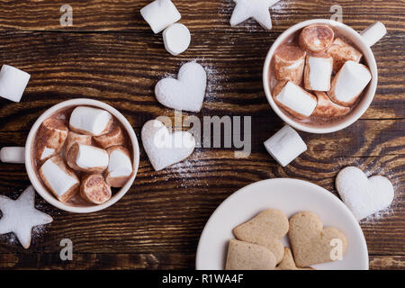 Biscuits de Noël plaque saupoudrée de sucre en poudre et de tasses de chocolat chaud avec des guimauves sur table en bois, vue du dessus Banque D'Images