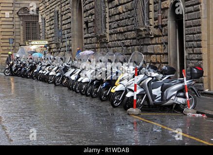 Rider sur le point de partir pour le plus éloigné d'une rangée de 27 scooters presque identiques en parallèle stationné humide des pluies, dans le centre de Florence, Italie Banque D'Images