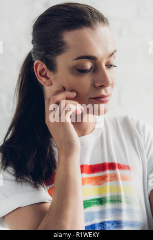 Close-up portrait of young transgenres homme en blanc T-shirt avec drapeau pride in front of white brick wall Banque D'Images