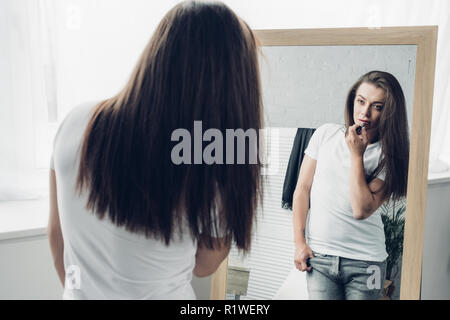Jeune homme transgenre appliquer le rouge à lèvres tout en regardant mirror Banque D'Images