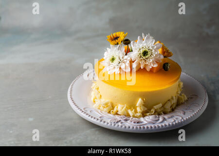 Cheesecake Mangue émaillés de fleurs et de morceaux de mangue fraîche sur fond gris Banque D'Images