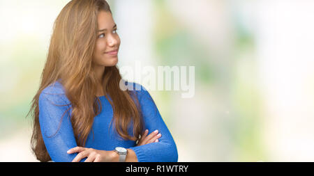 Jeune belle brunette woman wearing pull bleu sur fond isolé à sourire sur le côté avec les bras croisés convaincu et confiant Banque D'Images