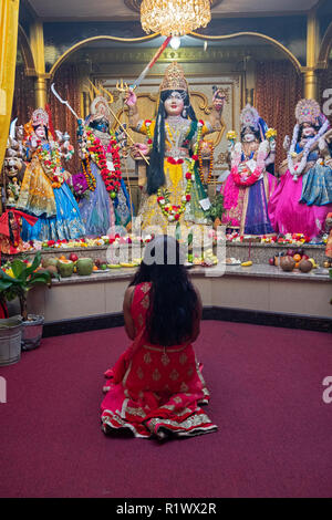 Une femme hindoue non identifiés s'agenouille dans la prière et la méditation en face des statues de divinités dans un temple dans le Queens, New York. Banque D'Images