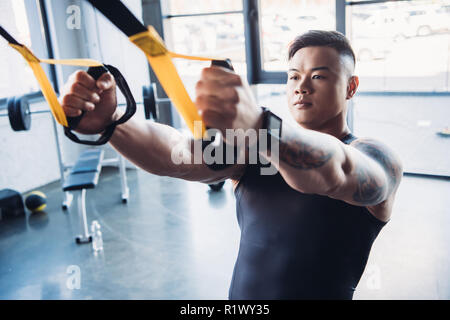 Jeune sportif musculaire ciblée formation avec bandes de résistance in gym Banque D'Images