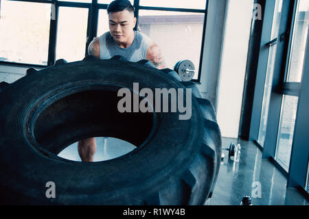 Les jeunes concentrés sportsman flipping tire lourd at gym Banque D'Images