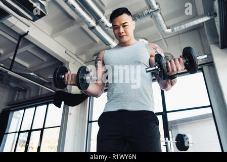 Jeune asiatique concentré sportsman l'entraînement avec haltères en salle de sport Banque D'Images