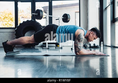 Side view of young sportsman faisant de l'exercice dans la salle de sport planche Banque D'Images