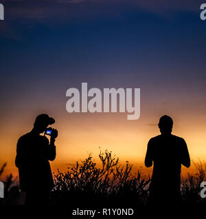Silhouette de deux hommes avec l'appareil photo au coucher du soleil Banque D'Images