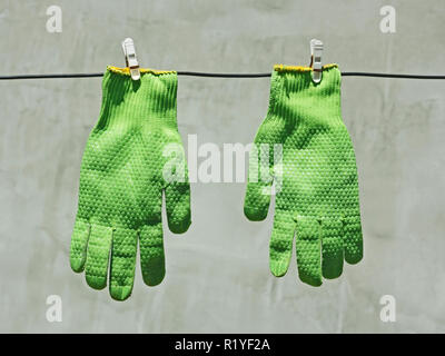 Deux gants vert bien accroché à un fil sur un fond de mur gris en plein soleil Banque D'Images