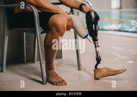 Cropped shot de sportif avec jambe artificielle assis sur une chaise à la piscine intérieure Banque D'Images