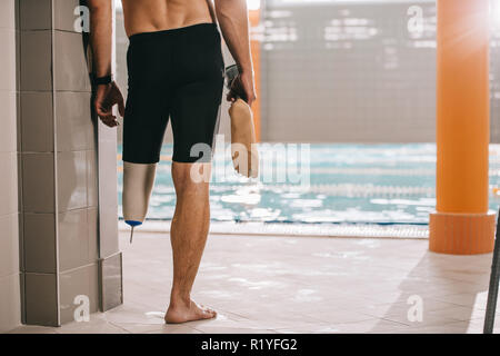 Cropped shot of athletic swimmer standing au bord de la piscine de piscine intérieure et tenant sa jambe artificielle Banque D'Images