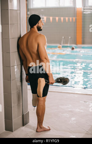 Vue arrière du jeune nageuse au bord de l'article piscine intérieure et tenant sa jambe artificielle Banque D'Images