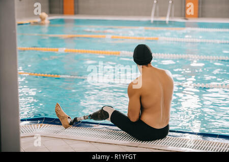 Vue arrière du jeune nageuse avec jambe artificielle assis sur de la piscine intérieure chauffée Banque D'Images