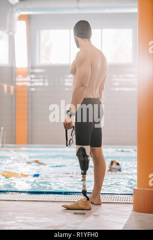 Beau jeune sportsman avec jambe artificielle debout devant une piscine intérieure Banque D'Images