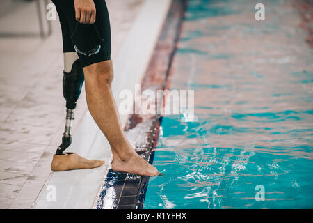 Cropped shot de monter nageur avec jambe artificielle à bord de piscine intérieure et contrôler la température de l'eau Banque D'Images