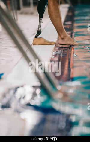 Cropped shot du nageur avec jambe artificielle à bord de piscine intérieure et contrôler la température de l'eau Banque D'Images