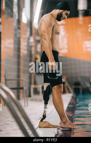 Beau jeune nageuse avec jambe artificielle à bord de piscine intérieure et contrôler la température de l'eau Banque D'Images