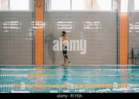 Beau jeune sportsman avec jambe artificielle à bord de piscine intérieure Banque D'Images