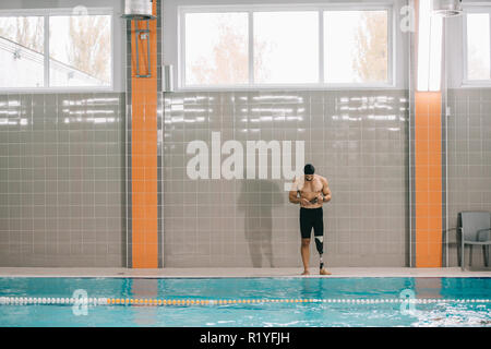 Beau jeune sportsman avec jambe artificielle à bord de piscine intérieure Banque D'Images