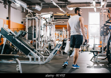 Beau jeune sportsman avec jambe artificielle debout à une salle de sport et une serviette holding Banque D'Images