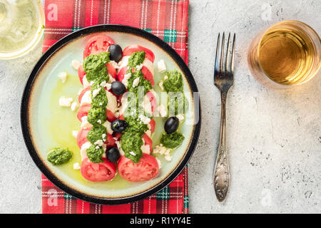 Salade caprese tomate et mozzarella et pesto aux olives de table gris servi avec serviette et verre rouge contrôlée vin blanc ou jus de pomme fourchette. Apéritif italien alimentaire Banque D'Images