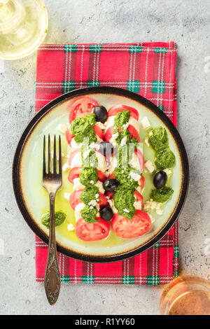 Salade caprese tomate et mozzarella et pesto aux olives de table gris servi avec serviette rouge vérifié, la carafe avec de l'huile d'olive et le verre de vin blanc ou de jus de pomme fourchette. Apéritif italien alimentaire Banque D'Images