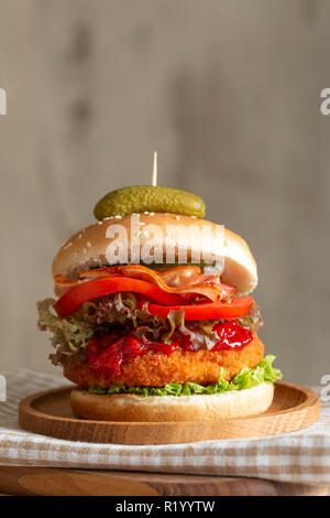 Burger avec les oignons, la laitue et les tomates sur une plaque de bois. Banque D'Images