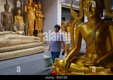 Un passant passe devant les statues de Bouddha sont placées à l'extérieur de l'usine d'un bouddha dans Bamrung Muang Road, Bangkok, Thaïlande Banque D'Images