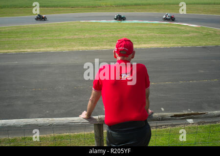 La course moto spectateur portant un Île de Man TT polo shirt et un bonnet rouge à Castle Combe, Wiltshire Banque D'Images