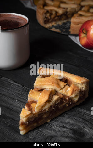 Vertical image avec une tranche de tarte aux pommes sur une table en bois rustique, une tasse de chocolat chaud et de l'ensemble de la tarte aux pommes. Des conditions de faible luminosité. Des desserts traditionnels. Banque D'Images