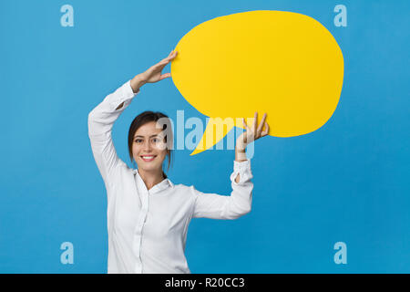 Happy brunette femme en chemise blanche élégante avec bulle jaune sur fond bleu Banque D'Images